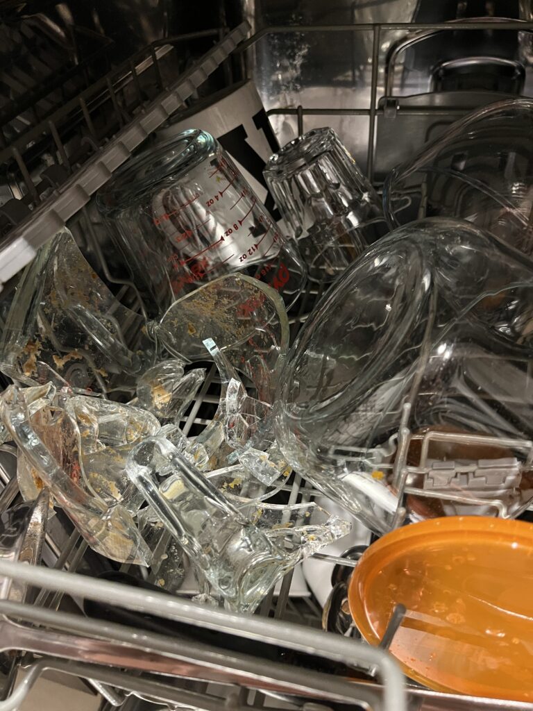 The top shelf of a dishwasher with a lot of glassware, including shards of a 1 litre pyrex jug that has self-destructed.