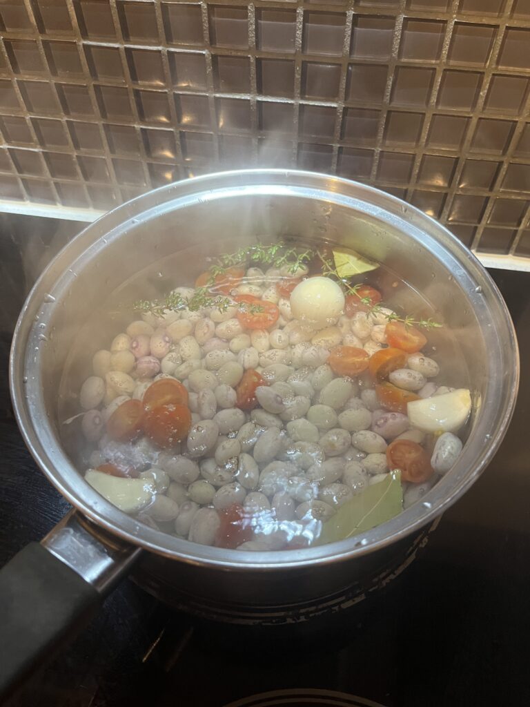 A saucepan containing borlotti beans, tomato, bay leaves, thyme and garlic